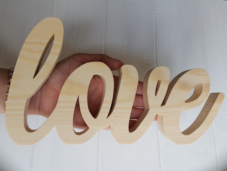 May include: A wooden sign spelling out the word "love" in a cursive font. The sign is made of light brown wood and has a natural finish.