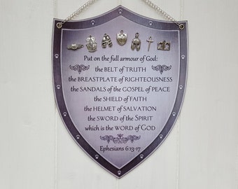 May include: A silver shield with a purple background and a quote from Ephesians 6:13-17 about the armor of God. The quote is surrounded by small silver charms representing the different pieces of armor.