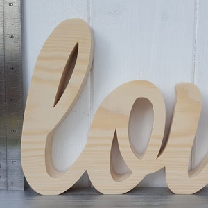 May include: Unpainted wooden word "love" in a cursive font. The letters are about 6 inches tall.