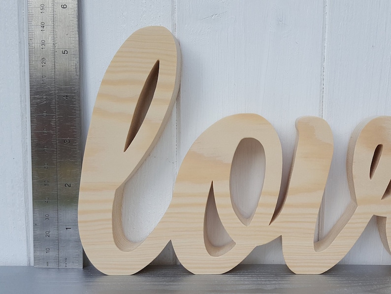 May include: Unpainted wooden word "love" in a cursive font. The letters are about 6 inches tall.