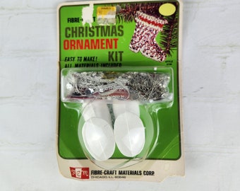 May include: A green and white Christmas ornament kit with a stocking design. The kit includes beads, string, and pins. The packaging says "Fibre-Craft Materials Corp. Chicago, Ill. 60646".