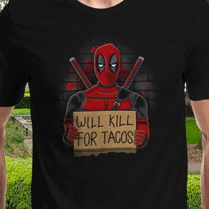 May include: A black t-shirt with a graphic of Deadpool holding a sign that says "Will Kill For Tacos".