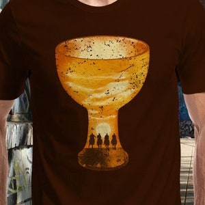 May include: A brown t-shirt with a graphic of a goblet filled with a sunset scene.  Silhouettes of four figures are visible at the bottom of the goblet.