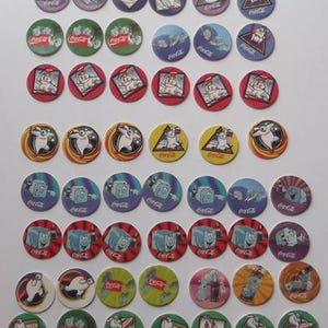 May include: A selection of colourful Coca-Cola pogs, each with a circular design and featuring cartoon characters. The pogs have various background colours, including red, green, purple, and yellow. Some pogs display the Coca-Cola logo.