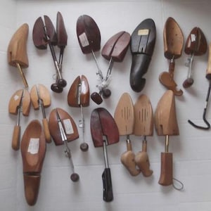 May include: A selection of wooden shoe trees in different designs. The shoe trees are crafted from light and dark brown wood, with metal and plastic parts. Some have adjustable features, while others are solid.