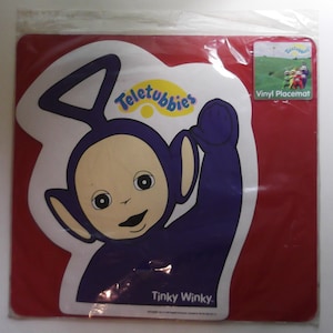 Könnte beinhalten: Eine rote Vinyl-Tischset mit Tinky Winky von den Teletubbies. Das Tischset hat eine weiße und lila Grafik von Tinky Winky mit dem Teletubbies-Logo. Der Text "Tinky Winky" ist unten aufgedruckt.