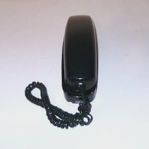 May include: A black, wall-mounted telephone with a coiled handset cord. The phone has a rectangular shape with rounded edges and a glossy finish. The cord is black and extends from the base of the phone.
