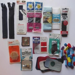 Peut inclure: Divers fournitures de couture, dont des fermetures éclair, du ruban thermocollant, de la tresse sergé, des boutons et du fil à broder. Les marques incluent Bondex, Scovill et Wrights. Diverses couleurs sont visibles, notamment le noir, le bleu, le blanc, le rouge et le rose.