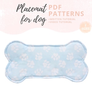 Op de afbeelding: Een lichtblauw, botvormig placemat voor honden met witte pootafdrukken. De tekst "Placemat for dog" staat linksboven, met "PDF PATTERNS" en "+WRITTEN TUTORIAL +VIDEO TUTORIAL" erboven. De tekst "2 SIZES" staat in een cirkel rechts.