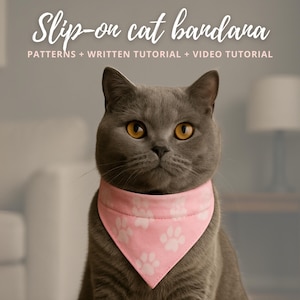 May include: A gray cat wearing a pink slip-on bandana with white paw prints. The text "Slip-on cat bandana" is at the top, with "PATTERNS + WRITTEN TUTORIAL + VIDEO TUTORIAL" below. The cat has yellow eyes.