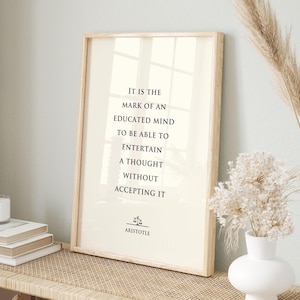 Könnte beinhalten: Ein rechteckiges gerahmtes Wandbild mit hellcremefarbenem Hintergrund und schwarzem Text: It is the mark of an educated mind to be able to entertain a thought without accepting it. Unter dem Text befindet sich ein kleines Waagensymbol und Aristotle.
