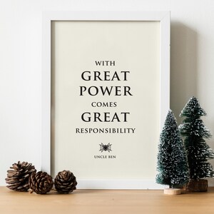 May include: A white framed wall art print featuring the black text WITH GREAT POWER COMES GREAT RESPONSIBILITY, with a small spiderweb icon and the words UNCLE BEN below. The print has a cream background and is displayed in a simple frame.