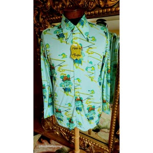May include: A light blue long-sleeved shirt with a colourful print of houses, trees, and horses. The shirt has a button-down collar and a pocket on the left side. The shirt has a tag that says "Styled by Montego".