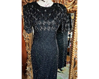May include: Black beaded dress with short sleeves and a round neckline. The dress features a diamond pattern on the upper bodice and a textured design on the skirt. The dress is displayed on a mannequin.