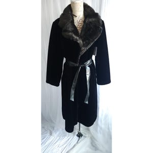 May include: A long, black coat with a faux fur collar and a matching belt. The coat is displayed on a mannequin. The faux fur collar is dark brown. The belt is tied at the waist. The coat is made of a soft, velvety material.