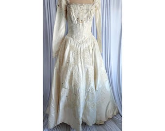 May include: Ivory-colored vintage wedding dress with long sleeves and a square neckline. The bodice is fitted and embellished with lace and sequins. The skirt is full, with intricate lace detailing. The dress is displayed on a mannequin.