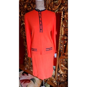 May include: A bright orange knit sweater and skirt set with black trim and buttons. The set is on a mannequin.