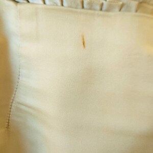 May include: Close-up of a cream-coloured fur coat lining. The lining is a light beige fabric with a small brown stain. The fur is a soft, fluffy texture.