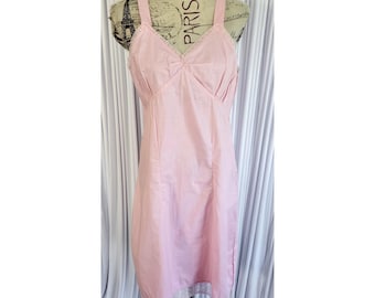 May include: A light pink slip dress with a V-neckline and spaghetti straps. The dress features a fitted bodice with pleats and a lace trim along the neckline and hem. The dress is displayed on a mannequin.