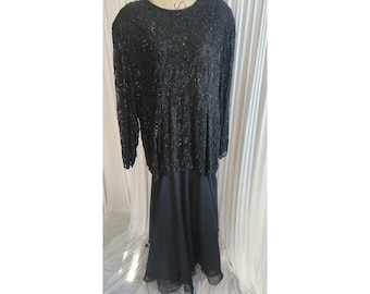 May include: A black formal dress with a beaded top and a long, flowing skirt. The top features intricate beadwork, and the skirt has a layered, sheer hem. The dress is displayed on a mannequin.