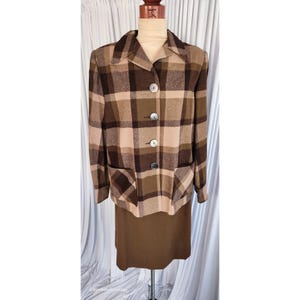 Könnte beinhalten: Ein zweiteiliger Vintage-Anzug mit einer karierten Jacke und einem passenden Rock. Die Jacke hat einen klassischen Kragen, drei Knöpfe und zwei Vordertaschen. Das Karomuster umfasst Brauntöne und Beige. Der Rock ist einfarbig braun.