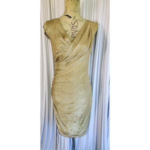 May include: A gold, sleeveless dress with a V-neck and draped fabric. The dress is displayed on a mannequin. The fabric has a textured, shimmering appearance. The dress is knee-length and form-fitting.