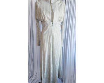 May include: A floor-length, long-sleeved dress in a shimmering silver fabric with a subtle vertical texture. The garment features a high collar, a fitted waistline with two small buttons, and a flowing skirt. The text Bombshellyvintage is visible.