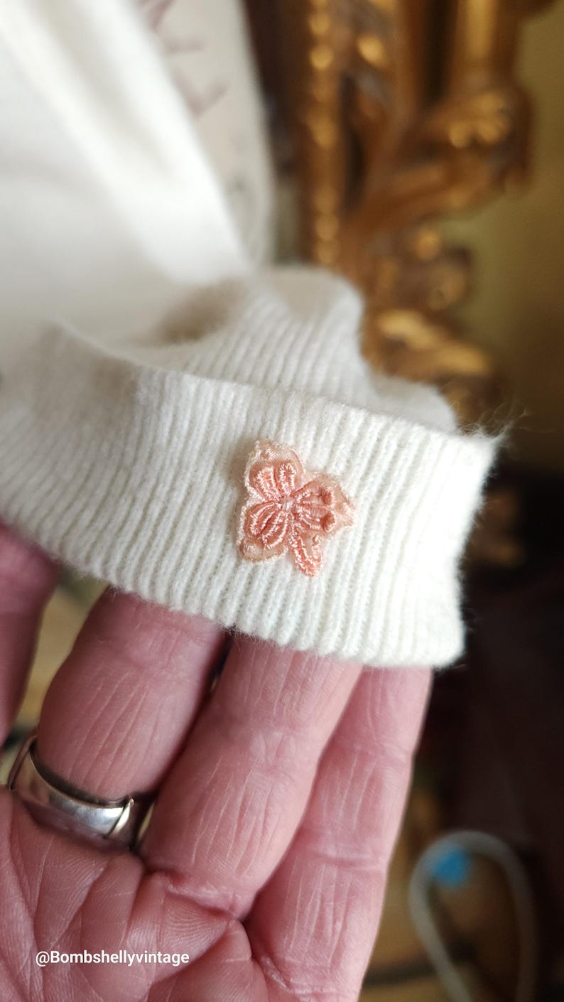 Puede incluir: Un su&eacute;ter de punto blanco con una flor rosa bordada en el pu&ntilde;o.