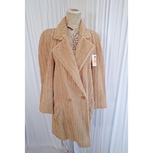 May include: A tan corduroy coat featuring a double-breasted front with two matching buttons, wide lapels, and long sleeves. The coat is displayed on a mannequin with a printed neck detail and a small white rectangular tag attached to the lapel.