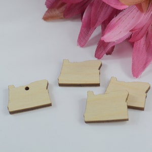 May include: Four unfinished wooden cutouts of the state of Oregon. The cutouts are on a white surface. One cutout has a small hole in the top.