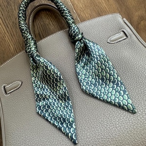 May include: A green and white patterned silk scarf tied around the handle of a brown leather handbag.