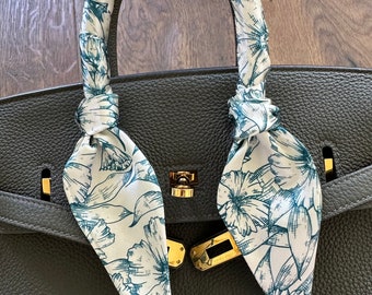 May include: A black leather handbag with a white and green floral patterned scarf tied around the handle.