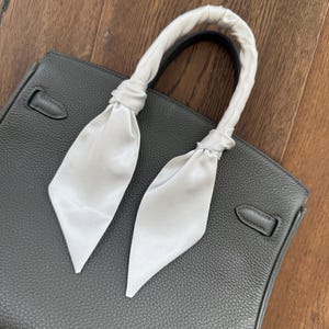 May include: A dark gray leather handbag with a white satin ribbon tied around the handles.