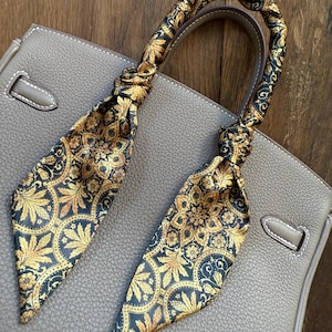 May include: A brown leather handbag with a gold and black patterned scarf tied around the handles.