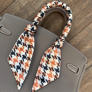 May include: A brown leather handbag with a black and orange patterned scarf tied around the handle.