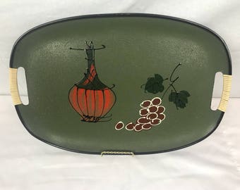 May include: A green oval serving tray with black trim and beige handles. The tray features a painted design of a red and orange bottle and a bunch of grapes.