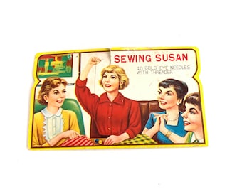 May include: A vintage sewing kit with a yellow background and an illustration of four women sewing. The text on the box reads "Sewing Susan 40 Gold Eye Needles with Threader".