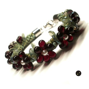 May include: A beaded bracelet with a silver clasp features a design of red and green flowers with white centres.