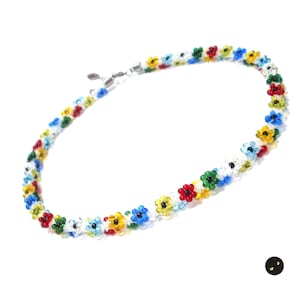 May include: A colourful beaded necklace featuring small flower-shaped beads in shades of red, yellow, blue, and green. The necklace is made of small glass beads and has a silver clasp.