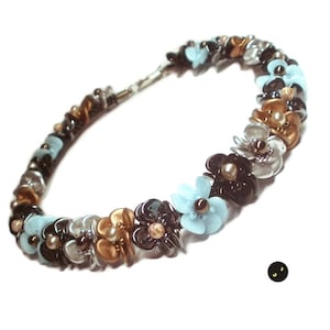 以下が含まれることがあります： 花柄のビーズネックレス。黒、白、金、水色のビーズが花の形に並んでいます。