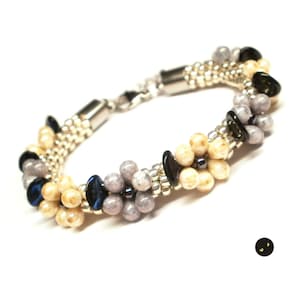 May include: A silver bracelet with a beaded design featuring cream, grey, and black beads. The beads are arranged in a floral pattern.