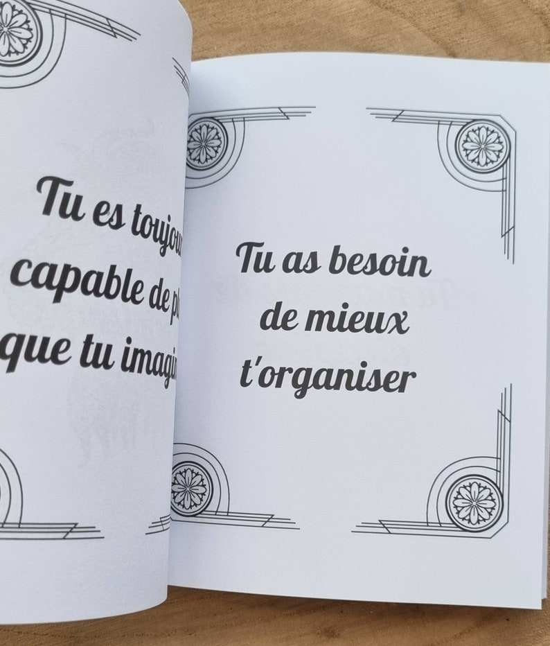Może przedstawiać: Otwarta książka z białymi stronami. Lewa strona zawiera tekst "Tu es toujours capable de plus que tu imagi". Prawa strona zawiera tekst "Tu as besoin de mieux t'organiser". Obie strony mają dekoracyjne czarno-białe wzory narożne.