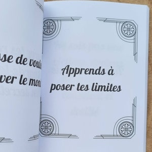 Może przedstawiać: Otwarta książka z tekstem "Apprends &agrave; poser tes limites" czcionką w kolorze czarnym. Strony są białe z dekoracyjnymi czarnymi wzorami w rogach. Książka leży na drewnianej powierzchni.