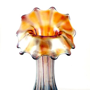 May include: An iridescent glass vase with a ruffled rim, showcasing shades of orange, purple, and blue. The vase has a slender, ribbed body. A silver fork is placed at the bottom of the image.