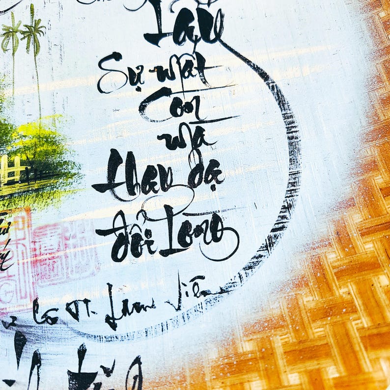 May include: Close-up of a painting with Vietnamese calligraphy in black ink on a light blue background. The painting has a woven bamboo border in shades of brown and yellow. The calligraphy is the focal point.