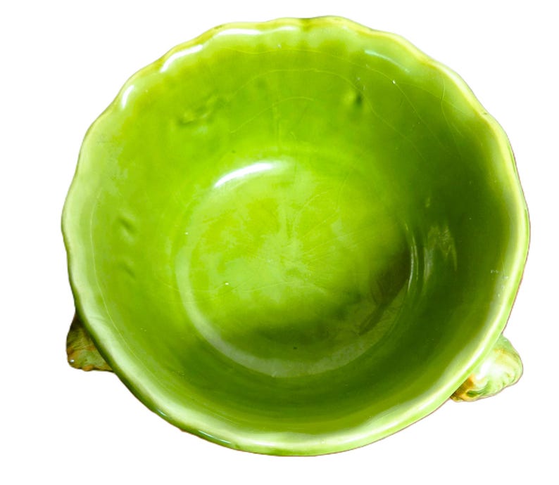 May include: A bright lime green ceramic bowl with a scalloped, wavy rim and a glossy, crackled glaze finish. The bowl features three small, textured, leaf-like feet extending from the base, providing a stable foundation for the rounded vessel.