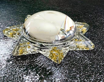May include: A clear glass star-shaped dish featuring a central circular dome and intricate gold-colored leaf patterns etched into the points of the star. The glass has a reflective surface and a smooth, polished finish throughout the design.