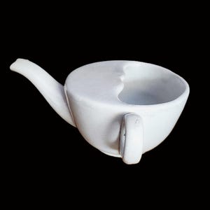 May include: A white ceramic teapot with a unique design. The teapot has a handle, a spout, and a curved rim. The teapot is set against a black background.