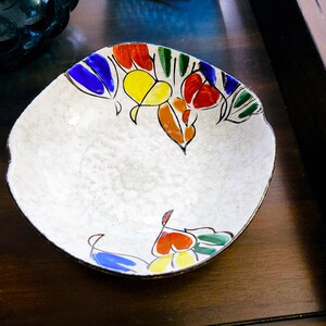 May include: A white ceramic bowl with a scalloped rim and a colorful floral design. The design features red, orange, yellow, blue, and green flowers and leaves.