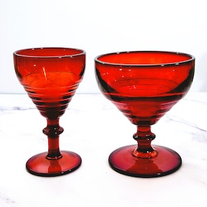 May include: Two red glass goblets with a fluted design. The goblets have a round base and a stem.